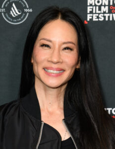 Lucy Liu smiling at red carpet event with long black hair and natural makeup
