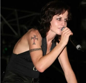 Dolores O’Riordan performing live with her distinctive red cross shoulder tattoo