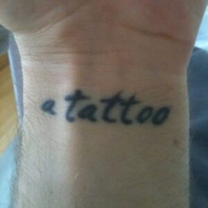 Close-up of Harry Judd’s wrist tattoo reading “a tattoo”