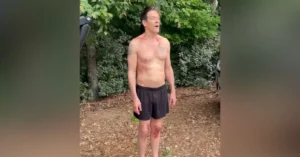 “Kevin Bacon shirtless with makeup bruises and shoulder tattoo during filming scene outdoors”